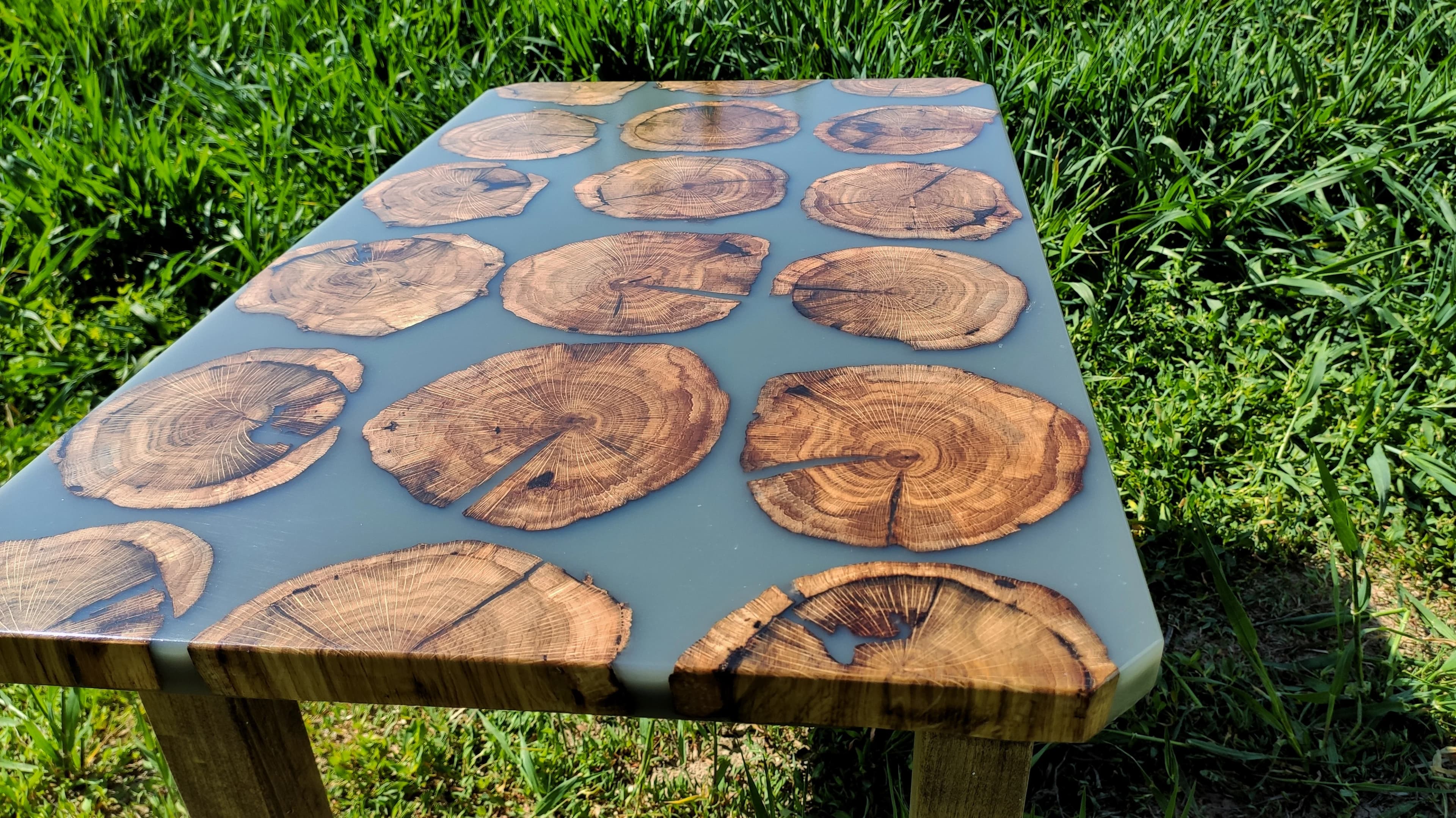 Mesa artesanal de rodajas de troncos naturales con resina azul perla sobre césped, Binéfar